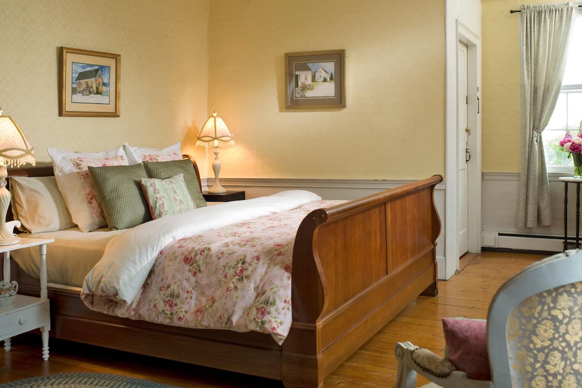A bedroom with a wooden bed, floral bedding, two bedside lamps, and two framed pictures on the wall.