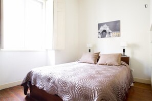 Uma cama bem arrumada com colcha estampada, um quadro na parede e uma mesa de cabeceira com abajur.