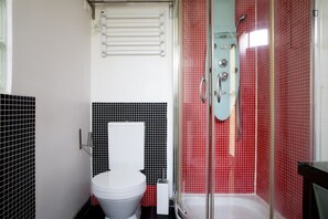 Ein Badezimmer mit einer weißen Toilette, einer Duschkabine aus Glas und roten Fliesen.