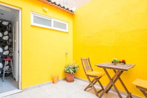 Eine kleine Terrasse mit einer gelben Wand, einem Holztisch, einem Stuhl, einem Blumentopf und einem Hocker.