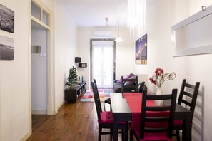Uma área de jantar com piso de madeira, uma mesa com toalha vermelha, cadeiras pretas e um vaso com flores.