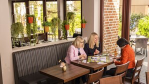 A restaurant with a brick wall, hanging plants, and a wooden bench. - Hotel Tiek.zwei (Meppen)