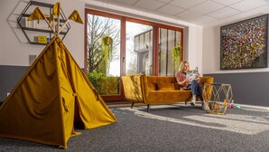 A room with a yellow tent, a sofa, and a person reading a book. - Hotel Tiek.zwei (Meppen)
