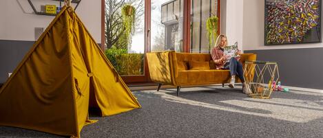 A room with a yellow tent, a sofa, and a person reading a book.