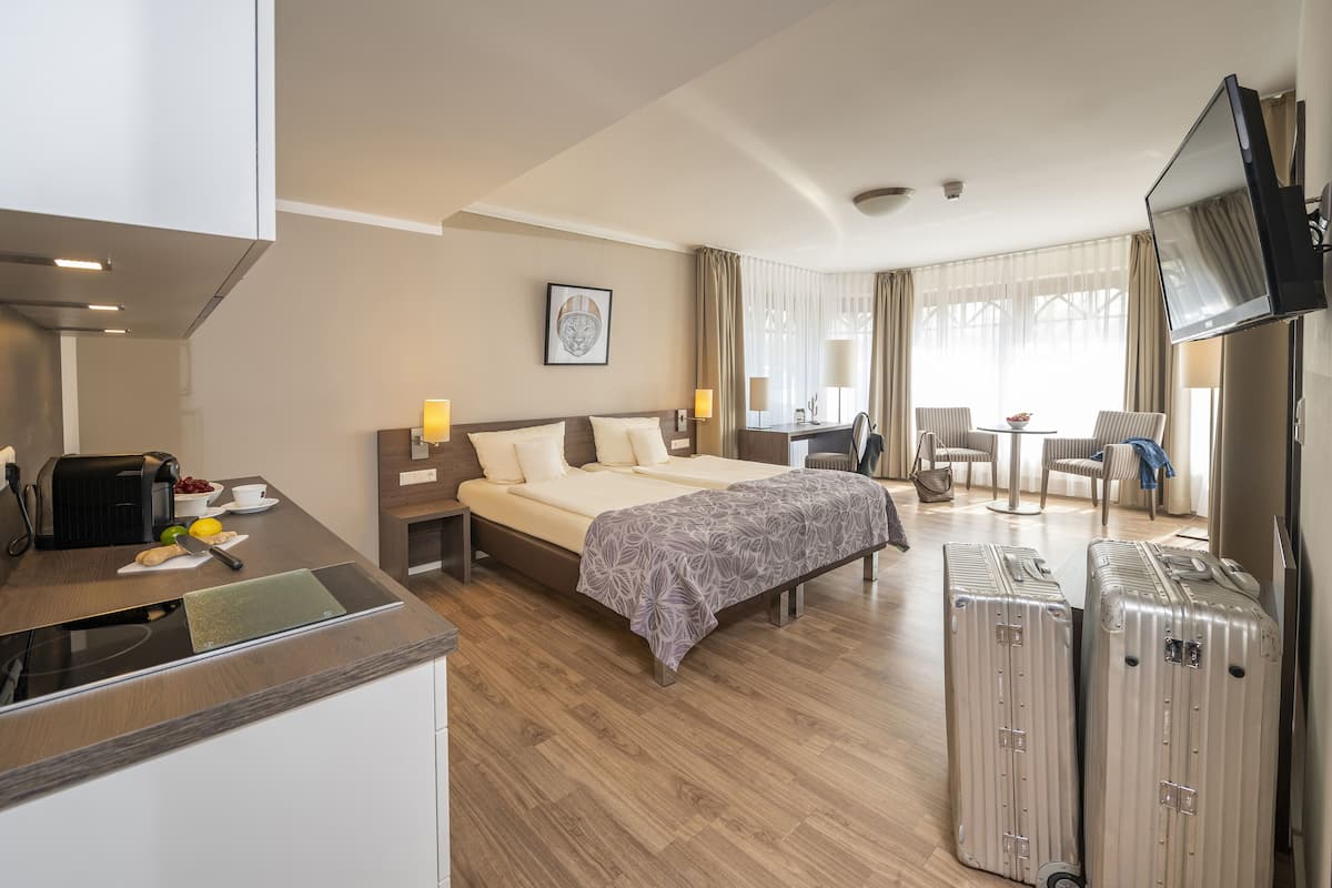 Una habitación de hotel con cama, mesita de noche, televisión, escritorio y dos maletas.