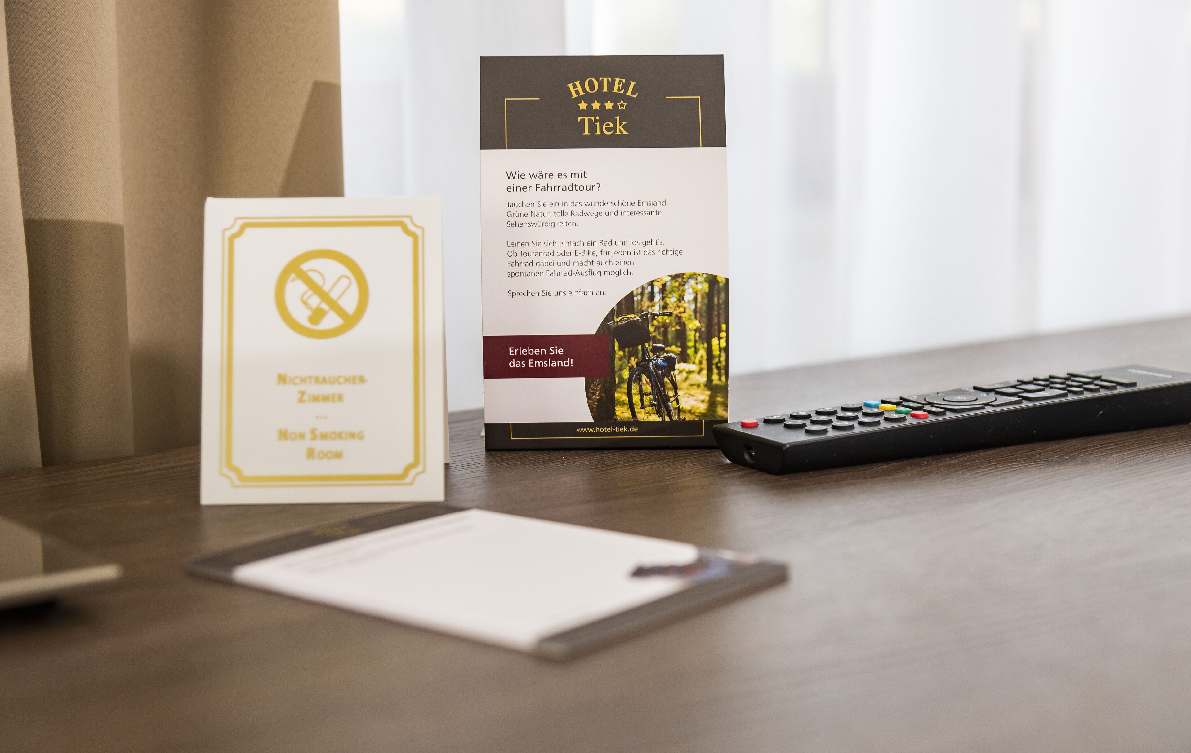 A hotel brochure, a non-smoking room sign, and a remote control on a wooden table.