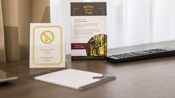 A hotel brochure, a non-smoking room sign, and a remote control on a wooden table.