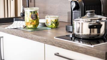 A kitchen with two glass jars of pickled vegetables on a countertop, a stainless steel pot, and a coffee machine.