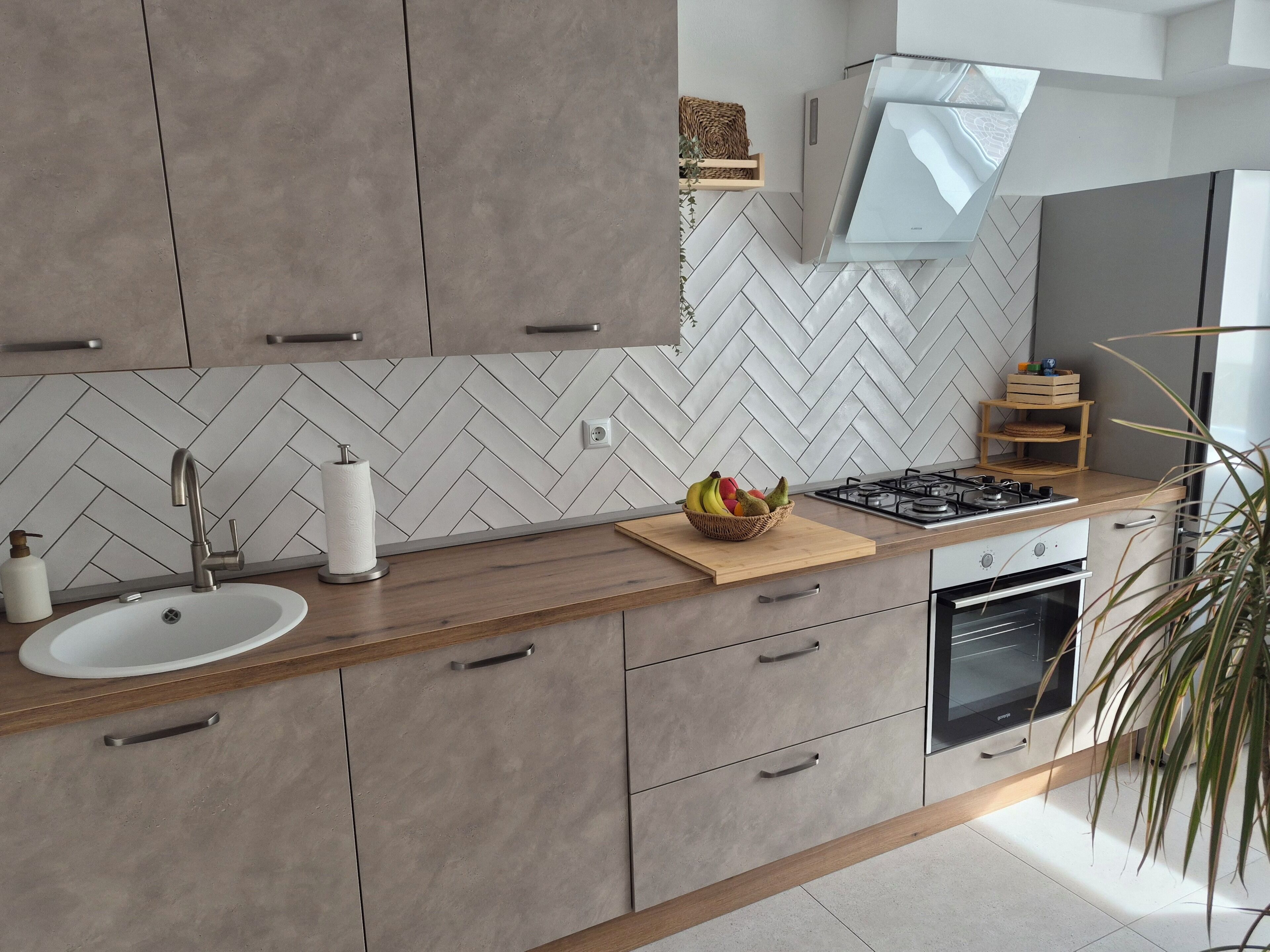Une cuisine moderne avec un dosseret de carreaux disposés en motif chevron, une cuisinière à gaz, un évier et des armoires en bois.