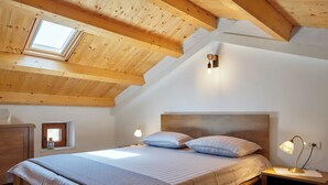 A bedroom with a sloped ceiling, wooden beams, a bed with two pillows, bedside lamps, and a small bedside table. - Holiday home Orihi * 2000 m2 fenced garden, covered terrace, BBQ (Barban)
