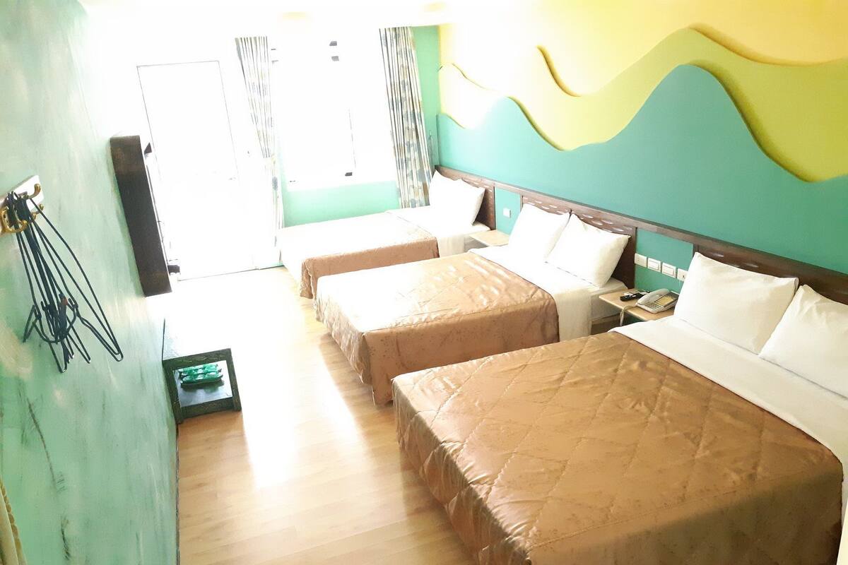 A hotel room with two single beds, a large bed, a wooden floor, and a view of the street.