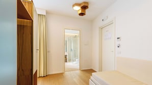 Un dormitorio moderno con un armario de madera, una cama y un baño visible a través de una puerta abierta.