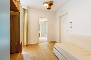 Una camera da letto moderna con un'armadio in legno, un letto e un bagno visibile attraverso una porta aperta.