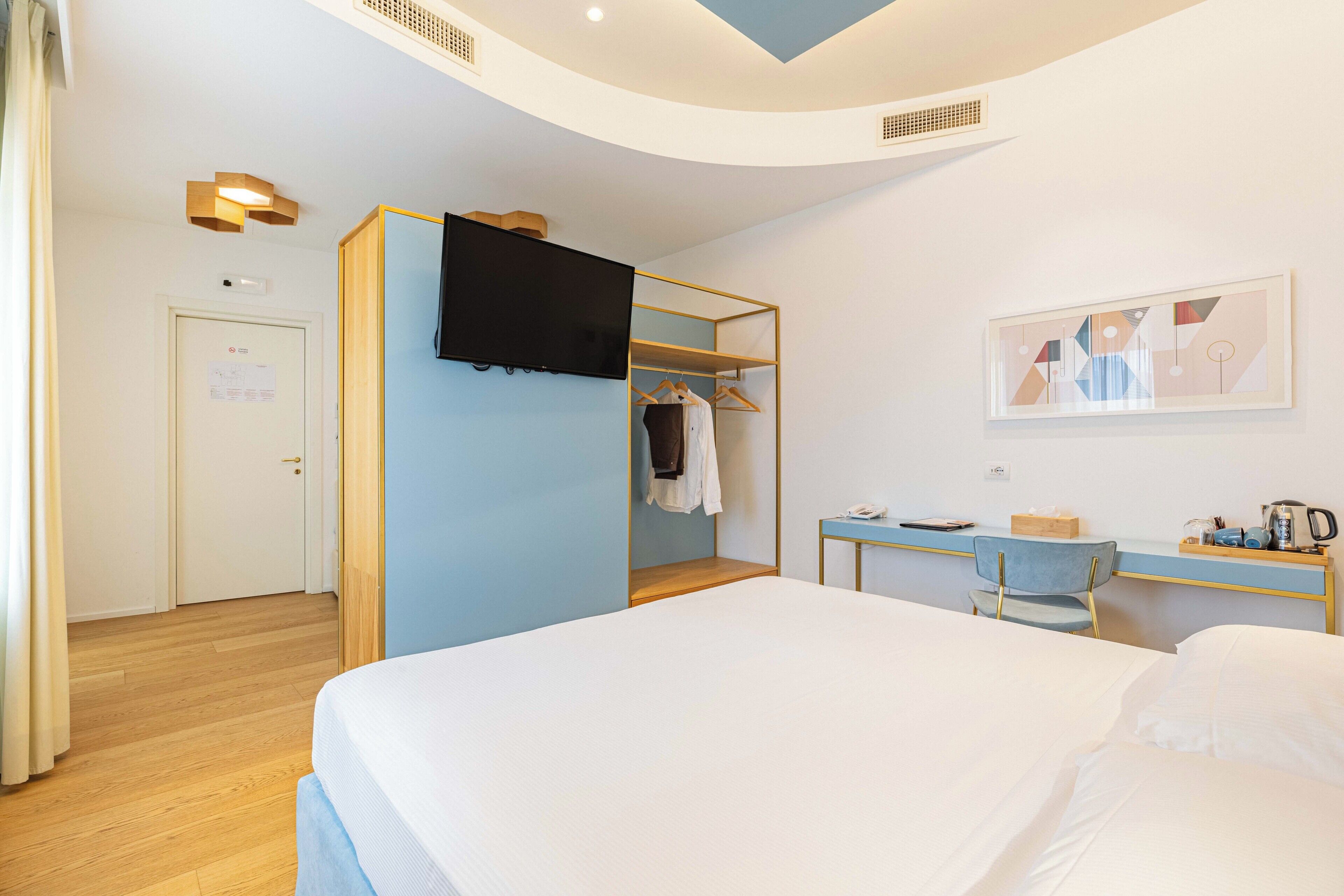 Une chambre d’hôtel moderne dotée d’un grand lit, d’un bureau avec une chaise, d’une armoire et d’un téléviseur à écran plat fixé au mur.