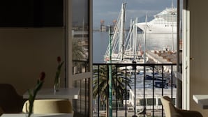 Una habitación moderna con un ventanal grande que da a un puerto deportivo con barcos y un crucero.
