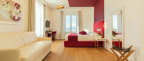 A modern hotel room with a large bed, a sofa, a desk, and a TV.