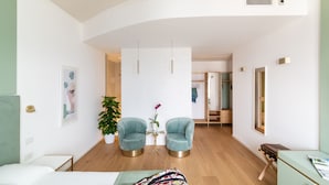Una habitación de hotel moderna con una cama, dos sillones, una mesita con una planta en maceta y un espejo grande.