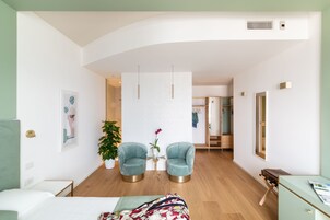 Una moderna camera d'albergo con un letto, due poltrone, un tavolino con una pianta in vaso e uno specchio grande.