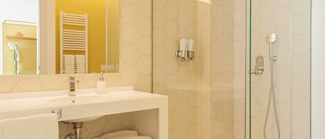 A bathroom with a glass-enclosed shower, a white sink with a mirror above it, and a hexagonal tile floor.