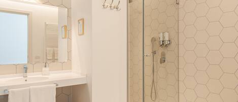 Un baño moderno con ducha de vidrio, lavamanos blanco con espejo y suelo de diseño hexagonal.