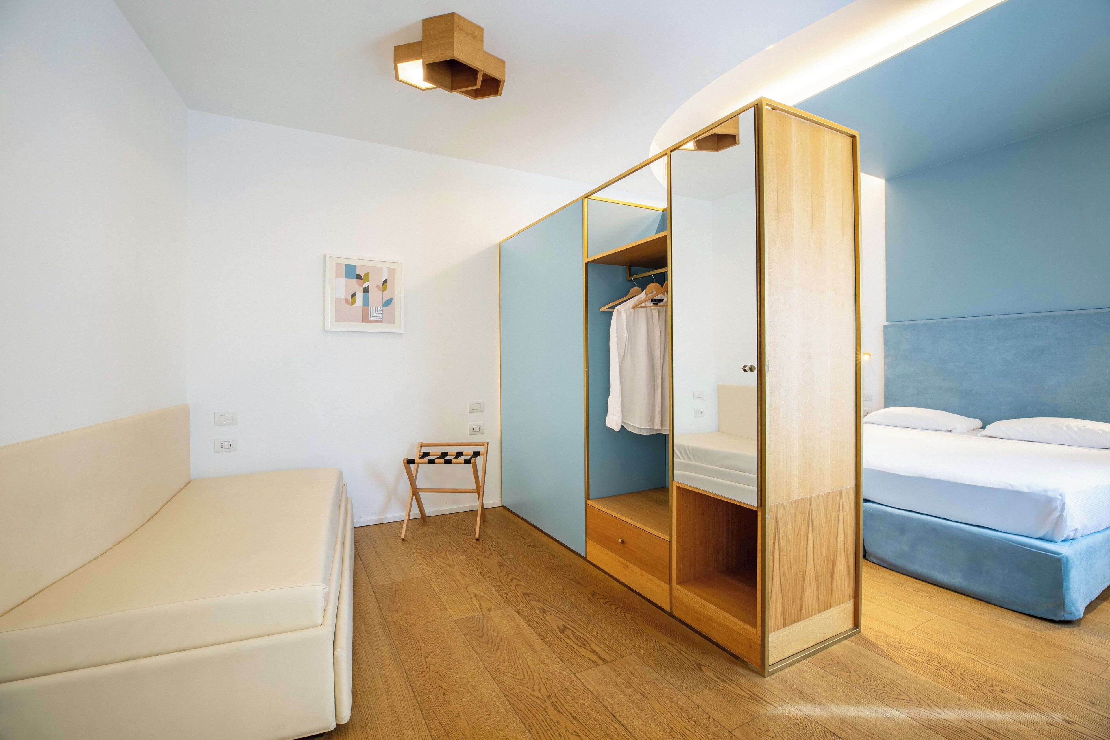 A modern bedroom with a bed, a wardrobe, and a small seating area.