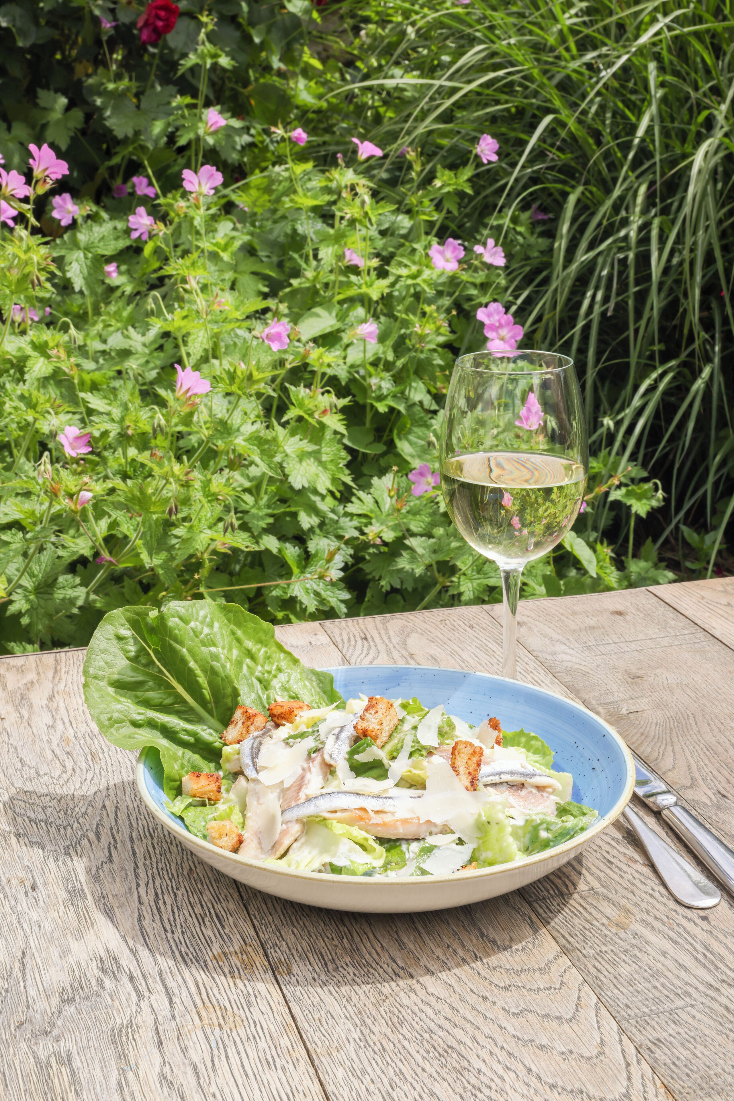 A salad with croutons and a glass of white wine on a wooden table.