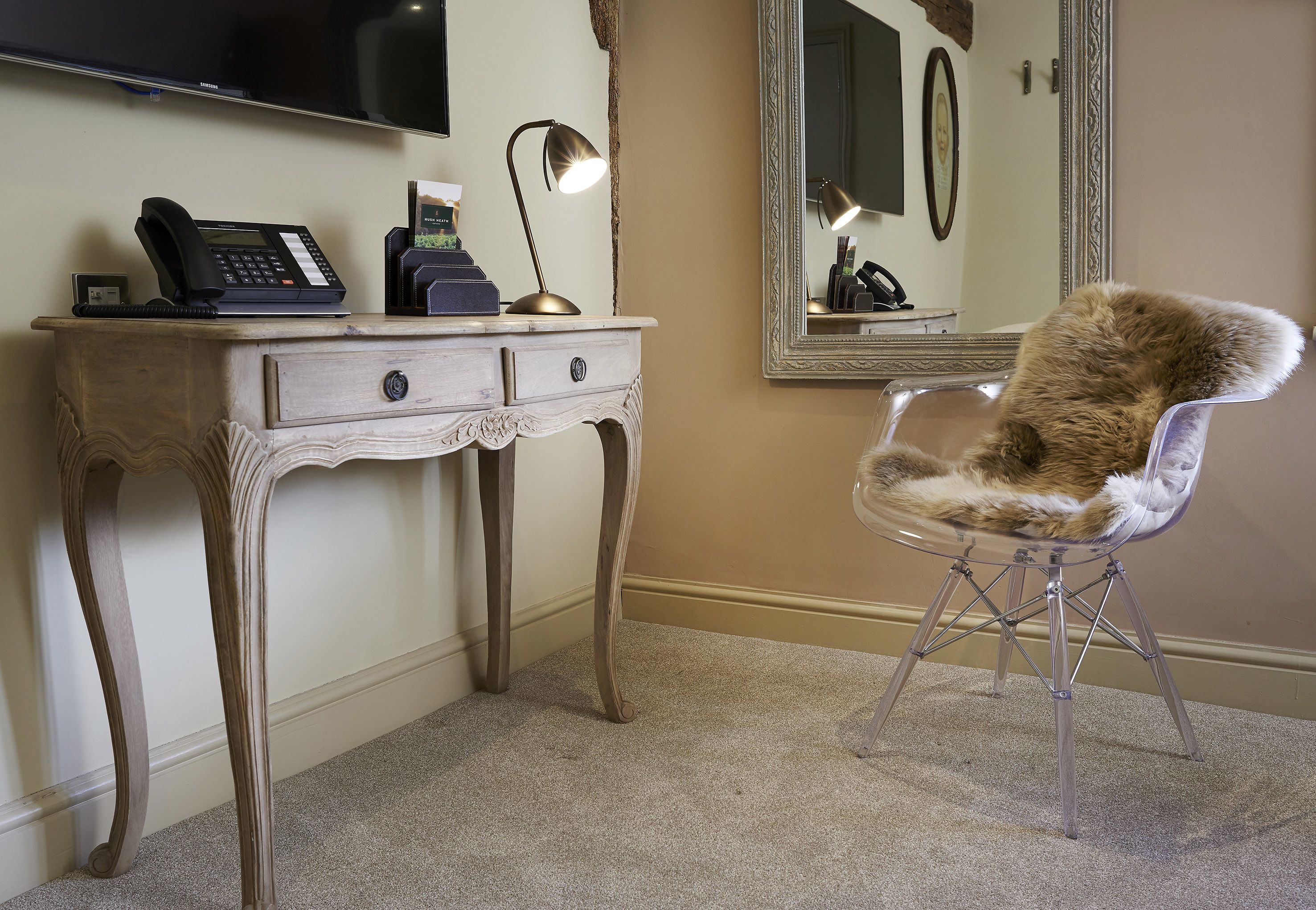 A room with a wooden desk, a telephone, a lamp, a mirror, and a fur chair.