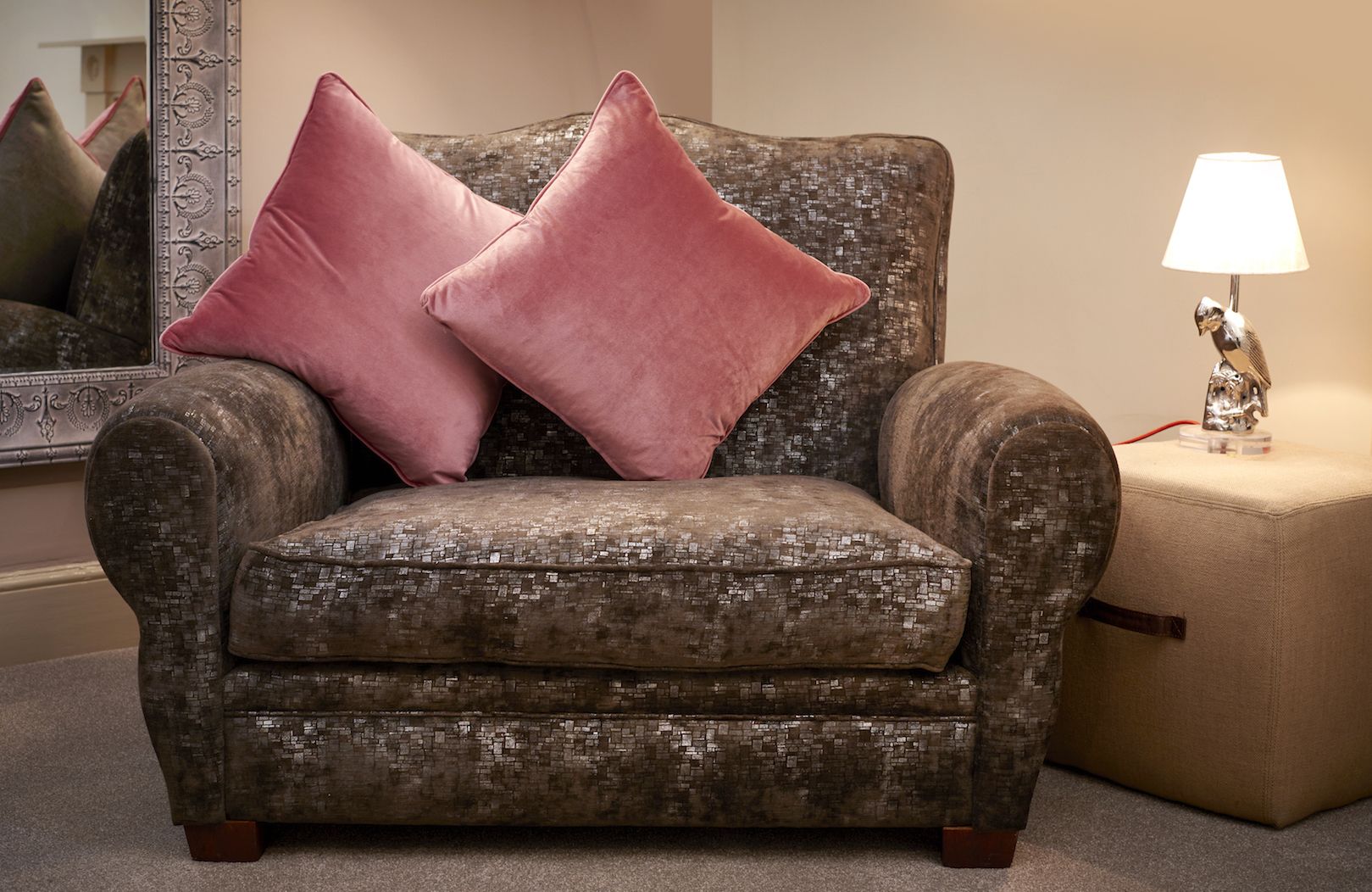 A tufted armchair with a textured fabric and two square cushions, positioned next to a lamp and a mirror on a carpeted floor.