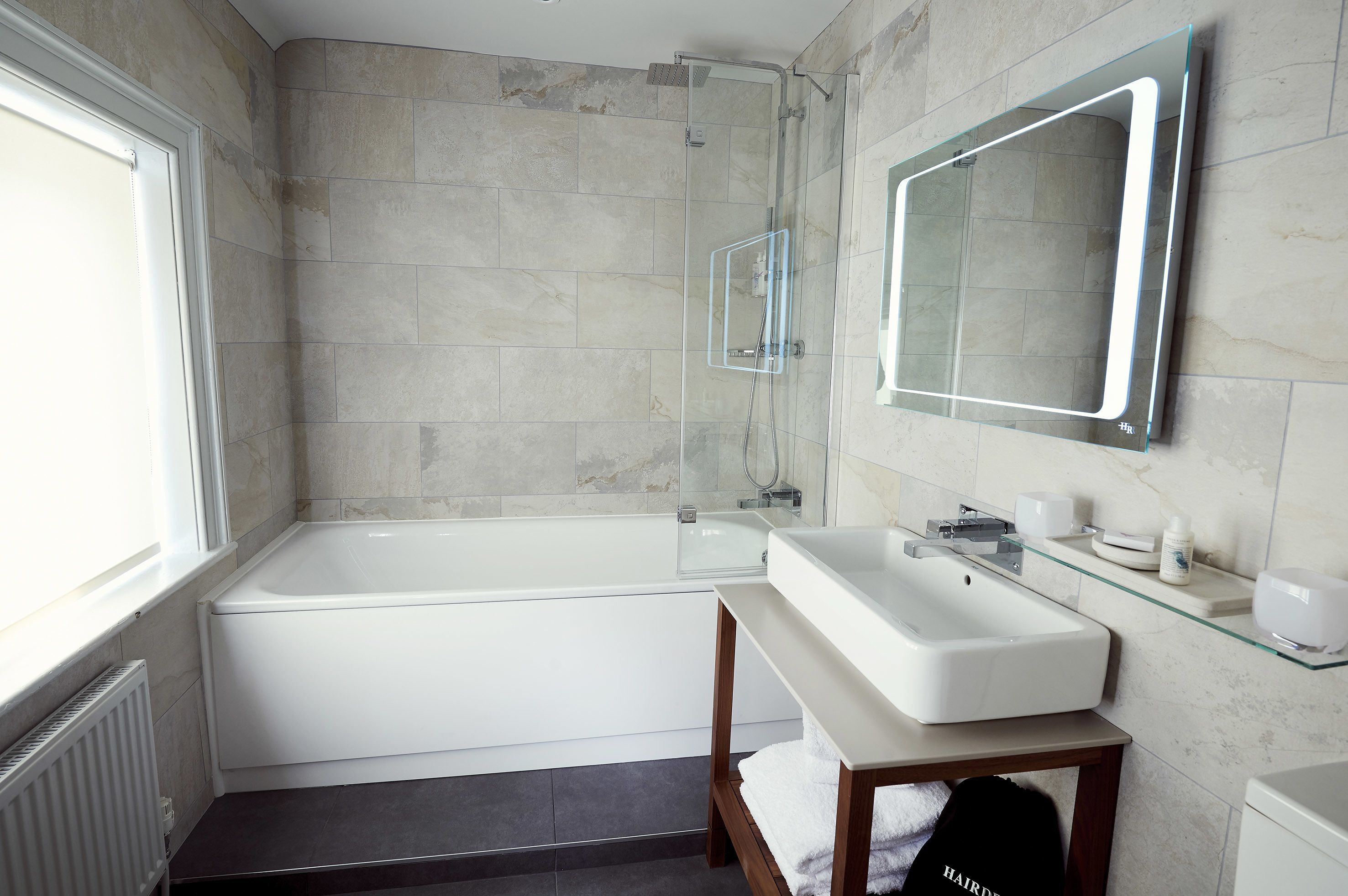 A modern bathroom with a glass-enclosed shower, a white bathtub, and a vanity with a mirror.