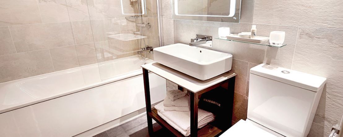 A modern bathroom with a freestanding sink, a glass shelf above the toilet, and a marble-tiled wall.
