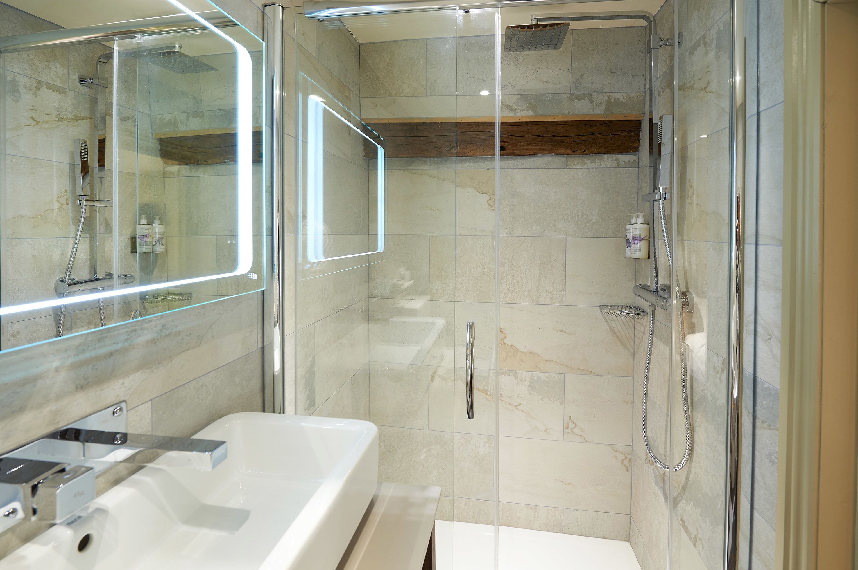A modern bathroom with a glass-enclosed shower, a large mirror, and a white sink.