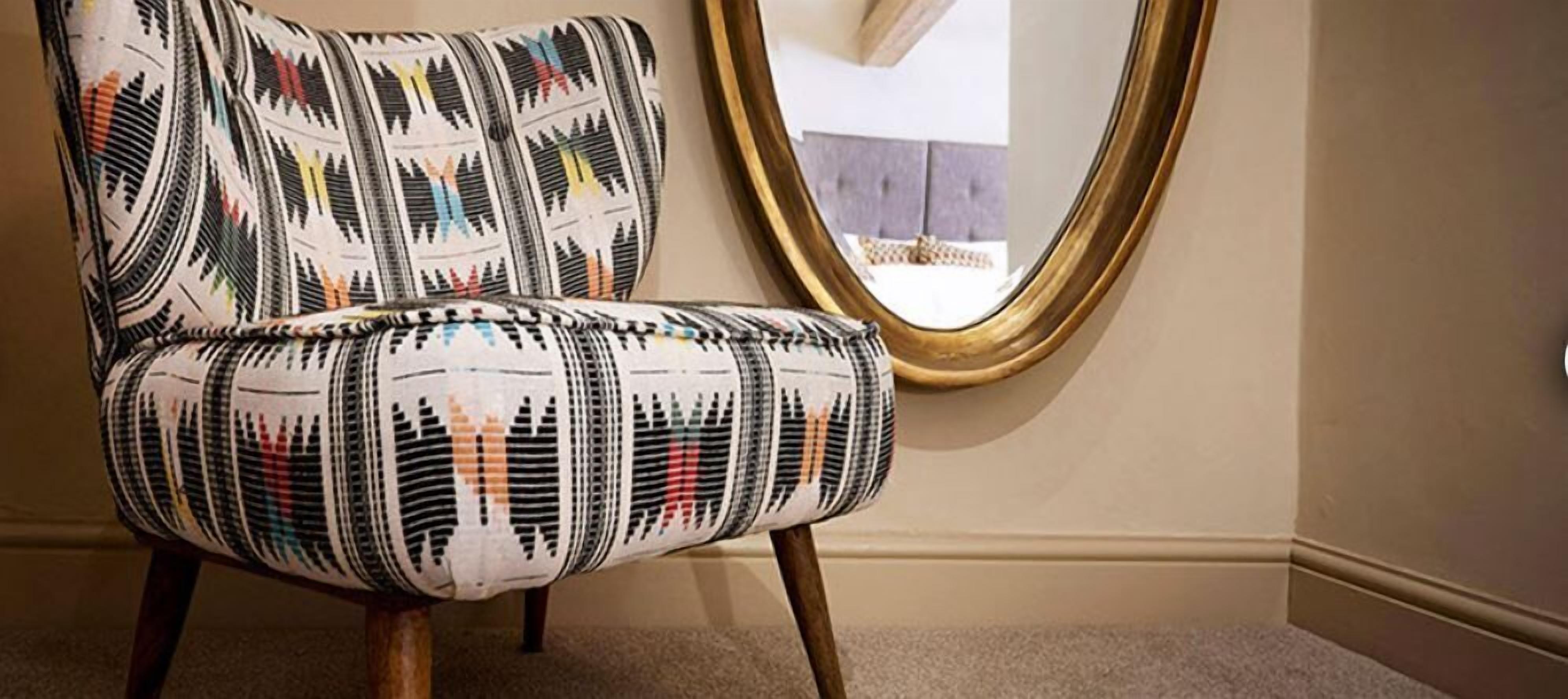 Una silla con tela estampada y patas de madera en una habitación con un espejo en la pared.