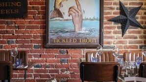 A restaurant interior with brick walls, wooden tables, and leather chairs. - The Tickled Trout (Maidstone)
