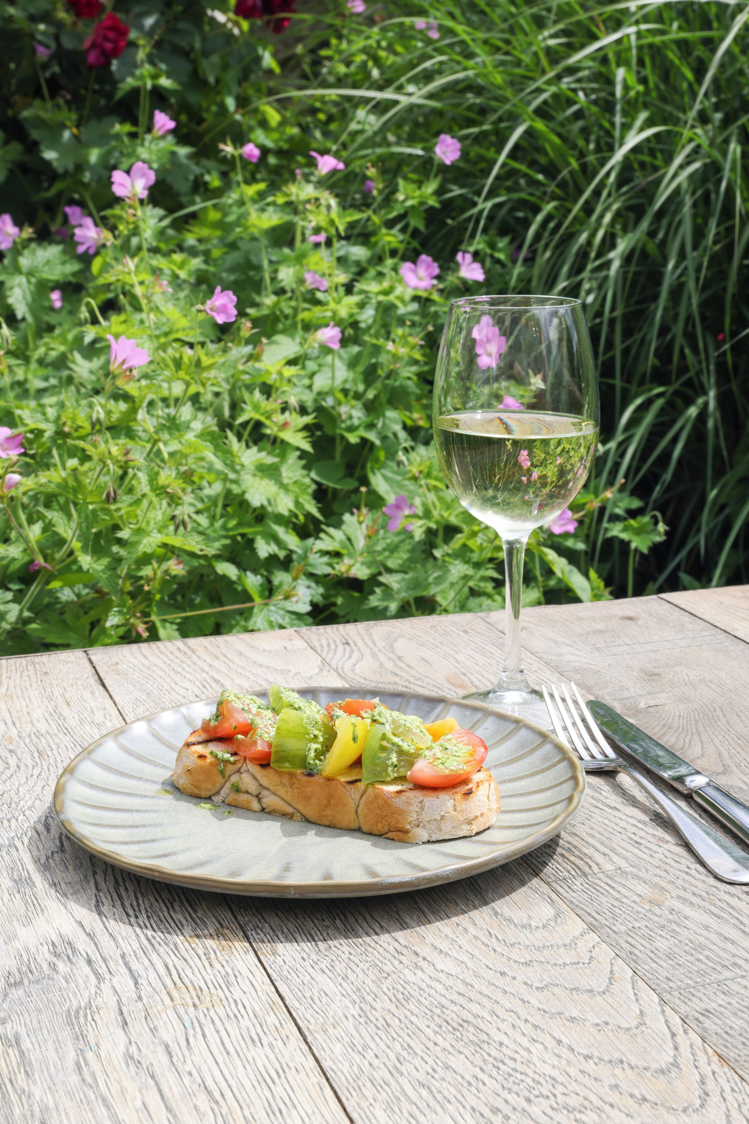 Une assiette avec un sandwich et un verre de vin blanc sur une table en bois.