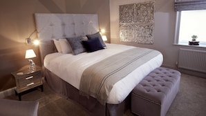 A neatly arranged bedroom with a large bed, bedside lamps, a decorative wall panel, and a window with a view. - The Tickled Trout (Maidstone)