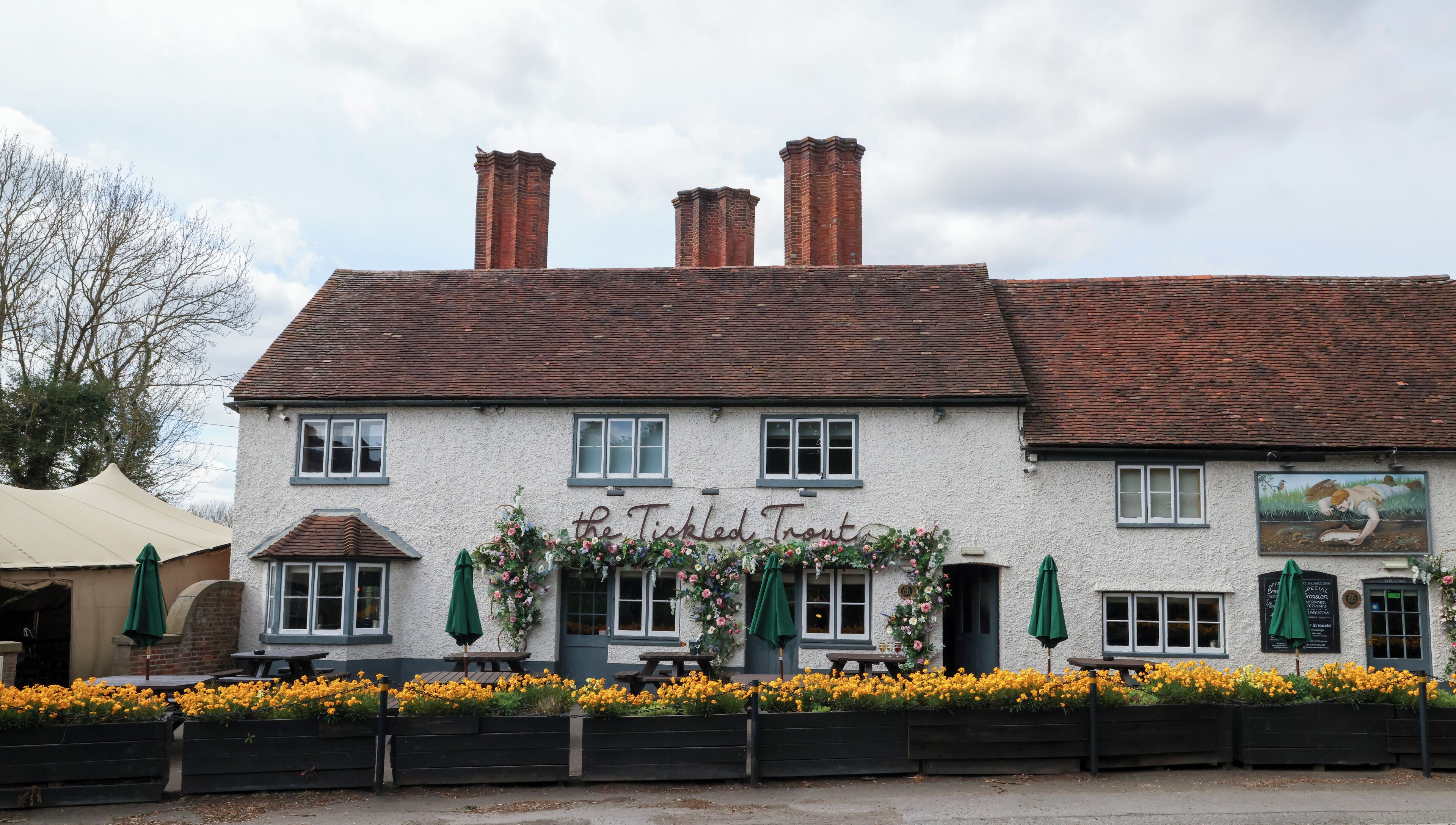A traditional pub with a white facade, multiple chimneys, and a sign reading "The Tickled Trout".