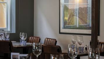 A restaurant with a table set for dining, a framed picture on the wall, and a window with a view of a vineyard.