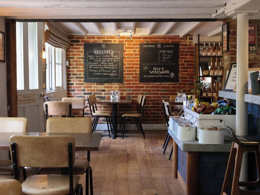 A cozy restaurant with brick walls, wooden tables, and chairs. There are chalkboards with specials and events listed.