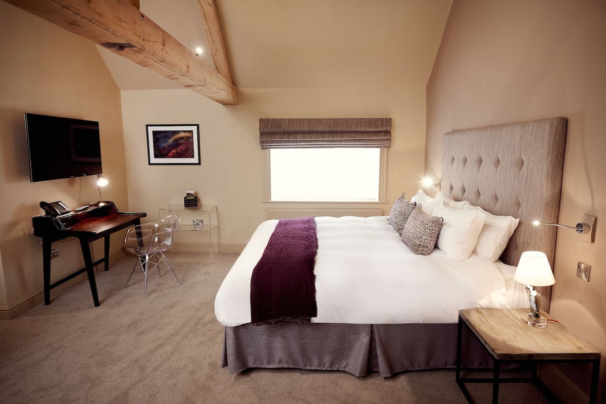 A bedroom with a large bed, a desk with a computer, a chair, a TV, and a window with curtains.