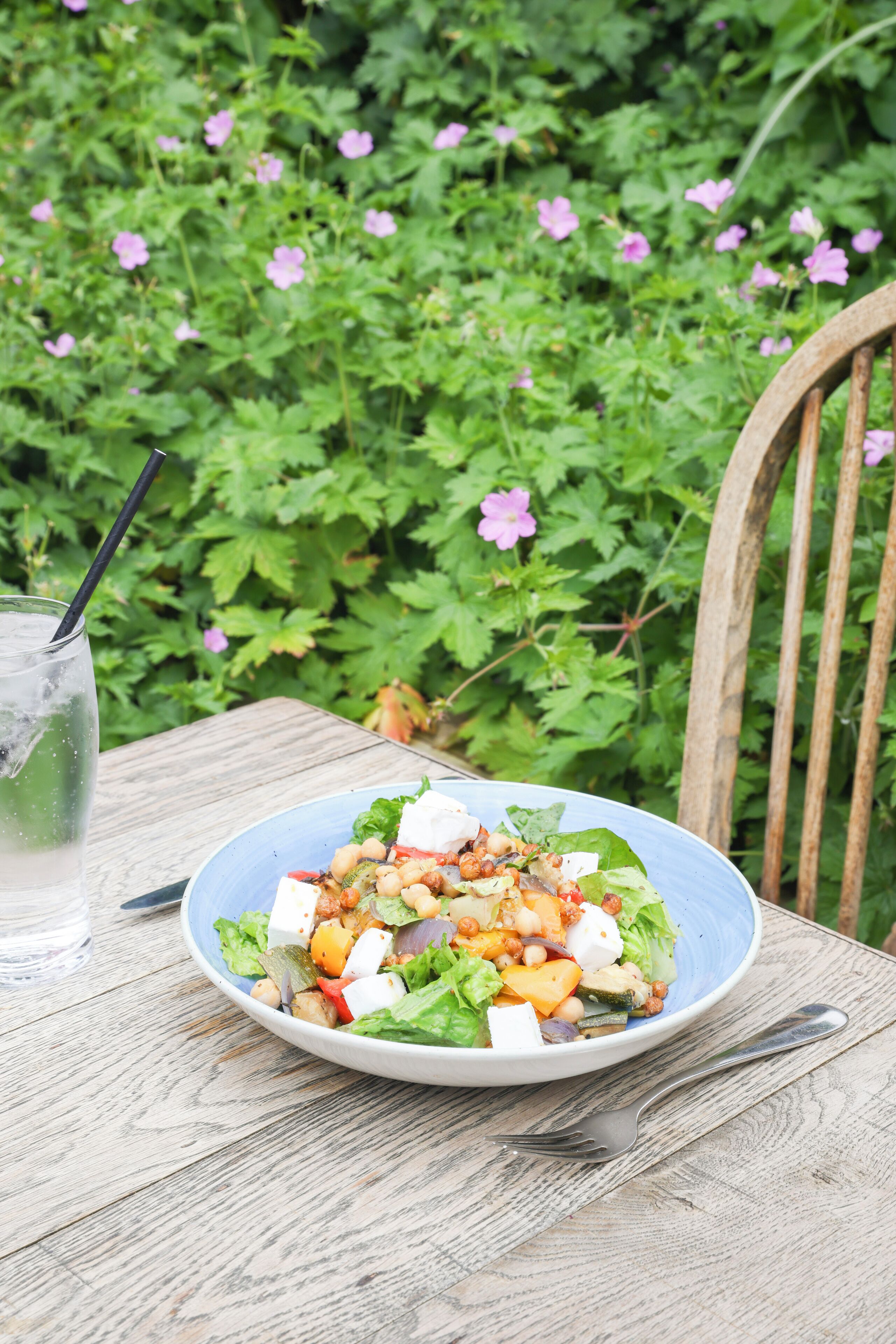 A table with a plate of salad, a glass of water, and a fork.