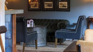 A cozy room with a dark blue sofa, a wooden table, and framed pictures on the wall. - The Tickled Trout (Maidstone)