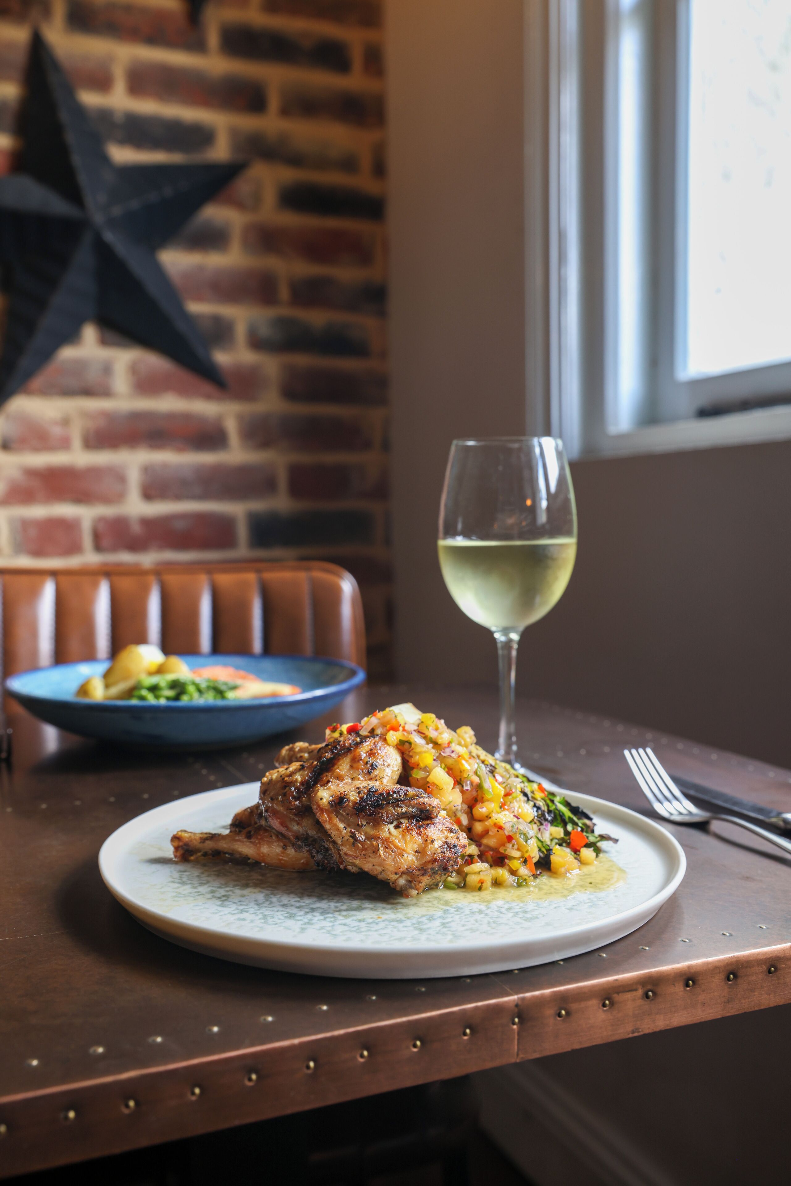 A dining table with a plate of food, a glass of white wine, and a star decoration on the wall.