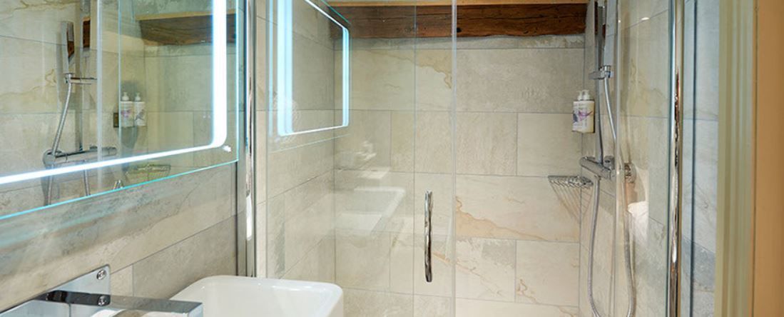 A modern bathroom with a glass-enclosed shower, a white bathtub, and a marble-tiled wall.