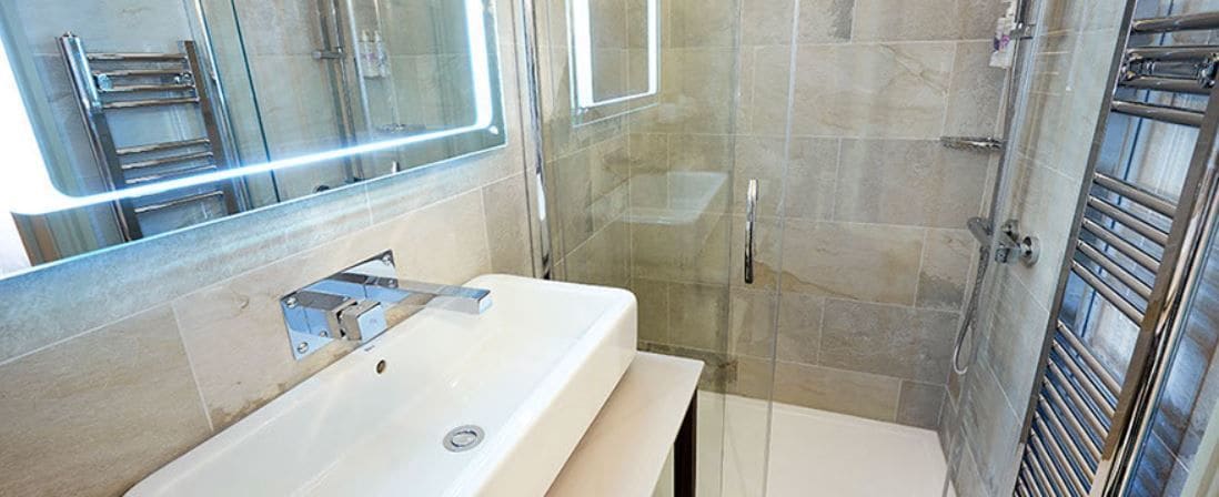 A modern bathroom with a glass shower enclosure, a white sink, and a mirror.