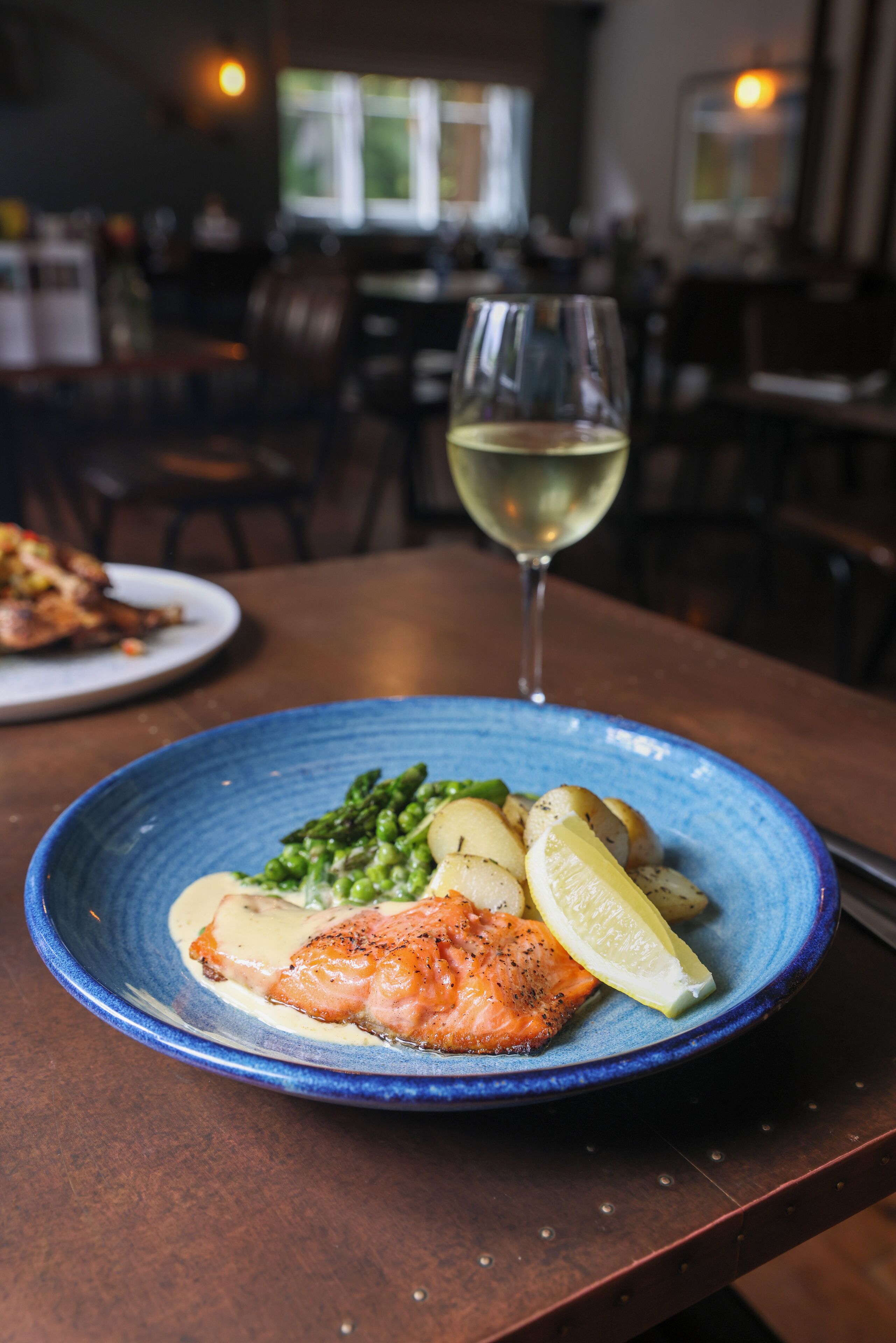 A plate of food with salmon, asparagus, and potatoes, and a glass of white wine on a wooden table.