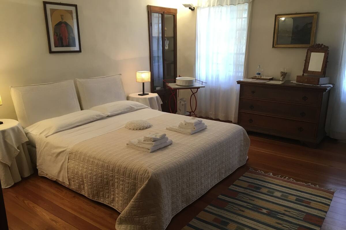 Un lit bien fait, avec des serviettes, une table de chevet avec une lampe, une commode et un miroir.