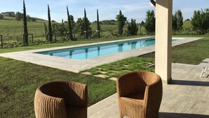 Une piscine surmontée d’une pergola, entourée de pelouse et d’arbres.