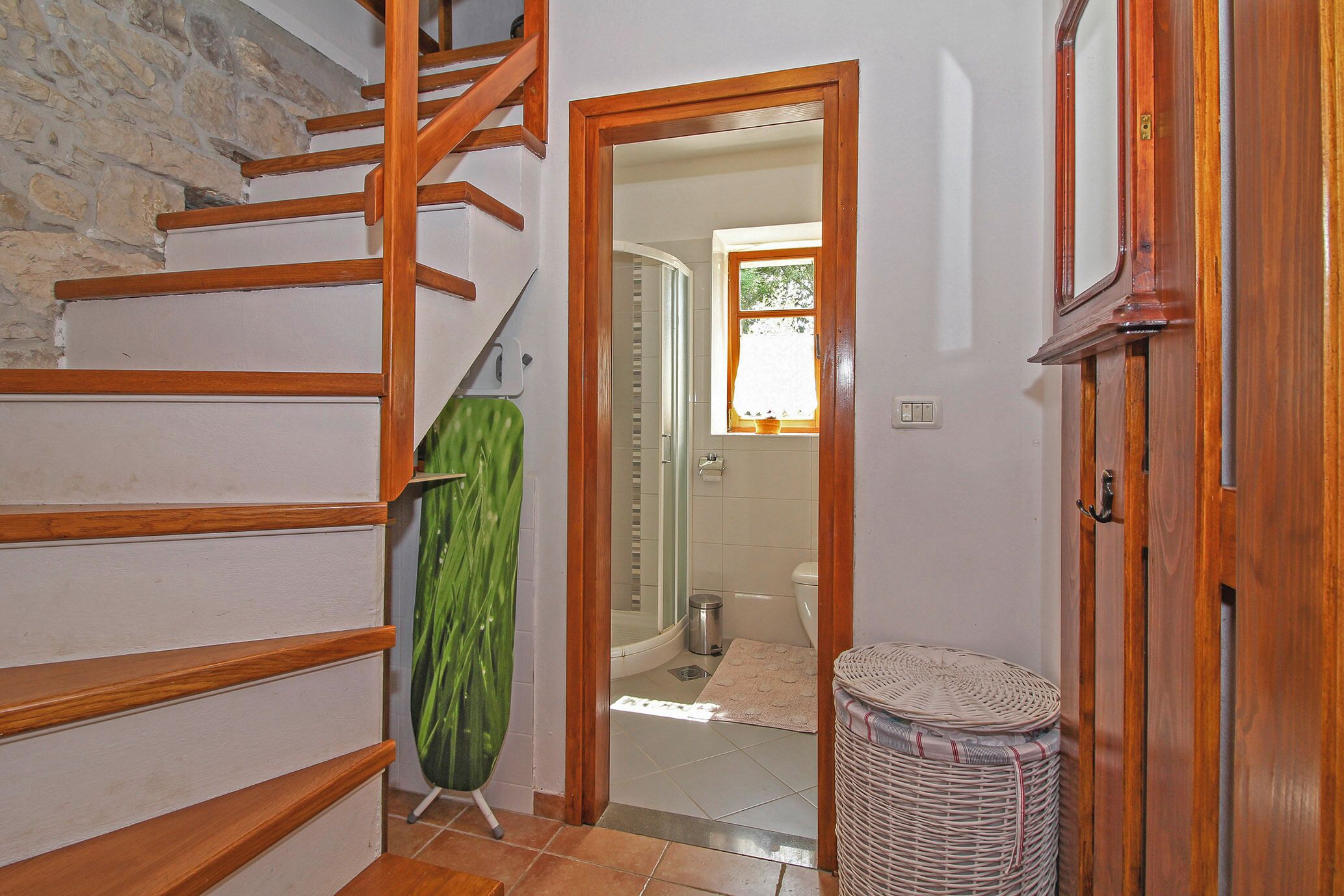 A staircase with wooden steps leading to a landing, a green umbrella, a wicker basket, and a bathroom with a shower and toilet visible through an open door.