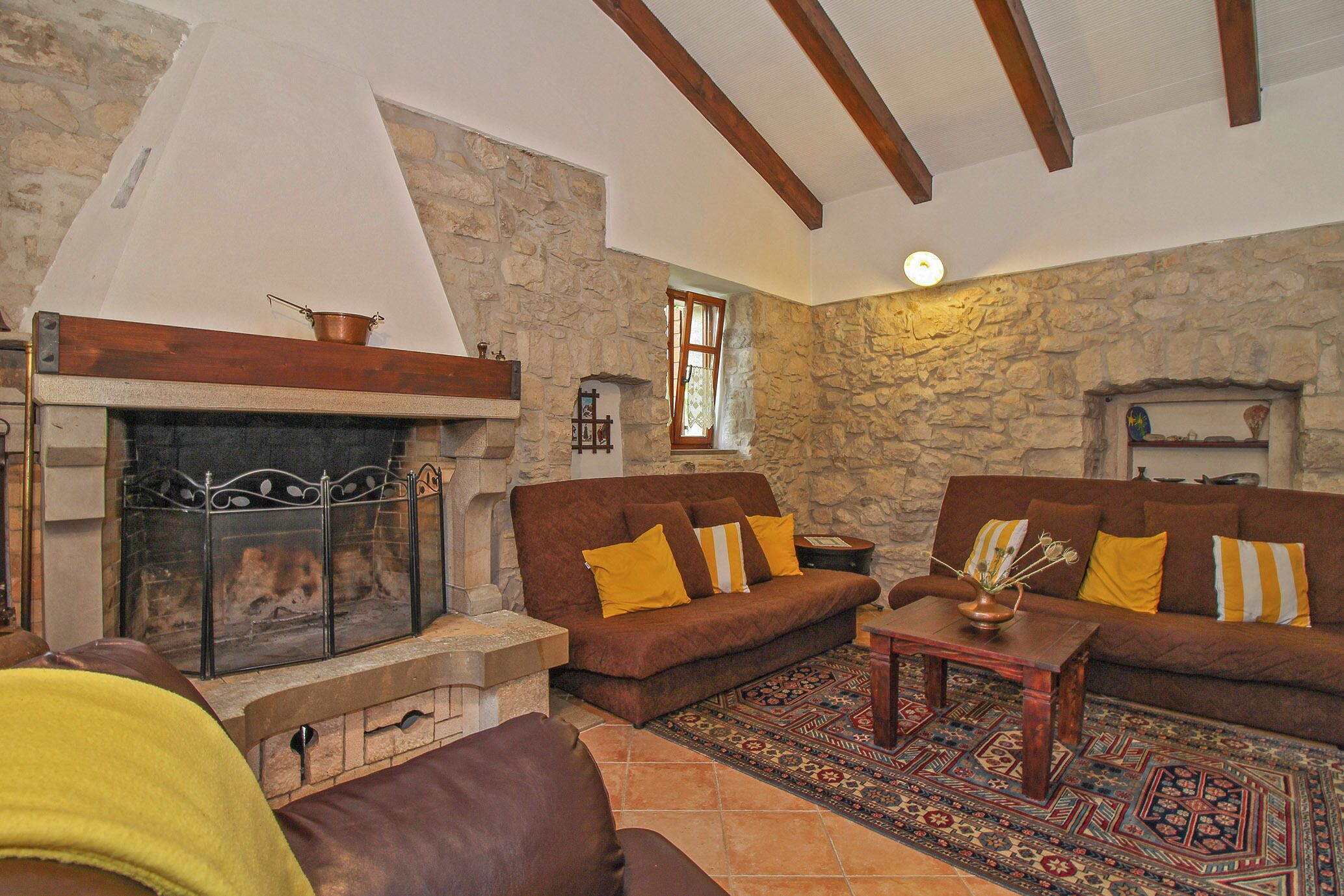 A cozy living room with a stone wall, a fireplace, and wooden beams.