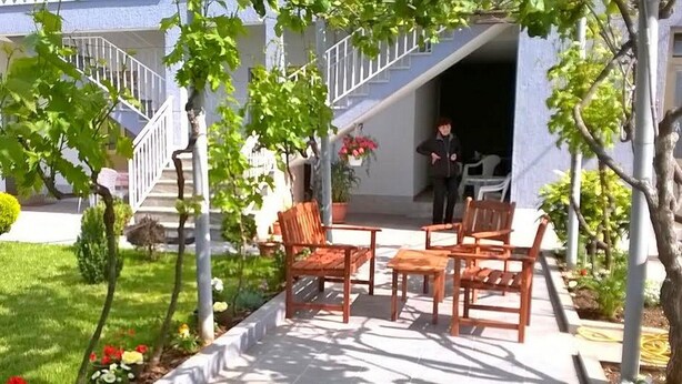 Un patio con mobiliario exterior, una escalera y un jardín con diversas plantas y flores.